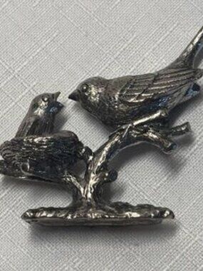 pewter figurine features a parent bird feeding a chick in a nest. high detail